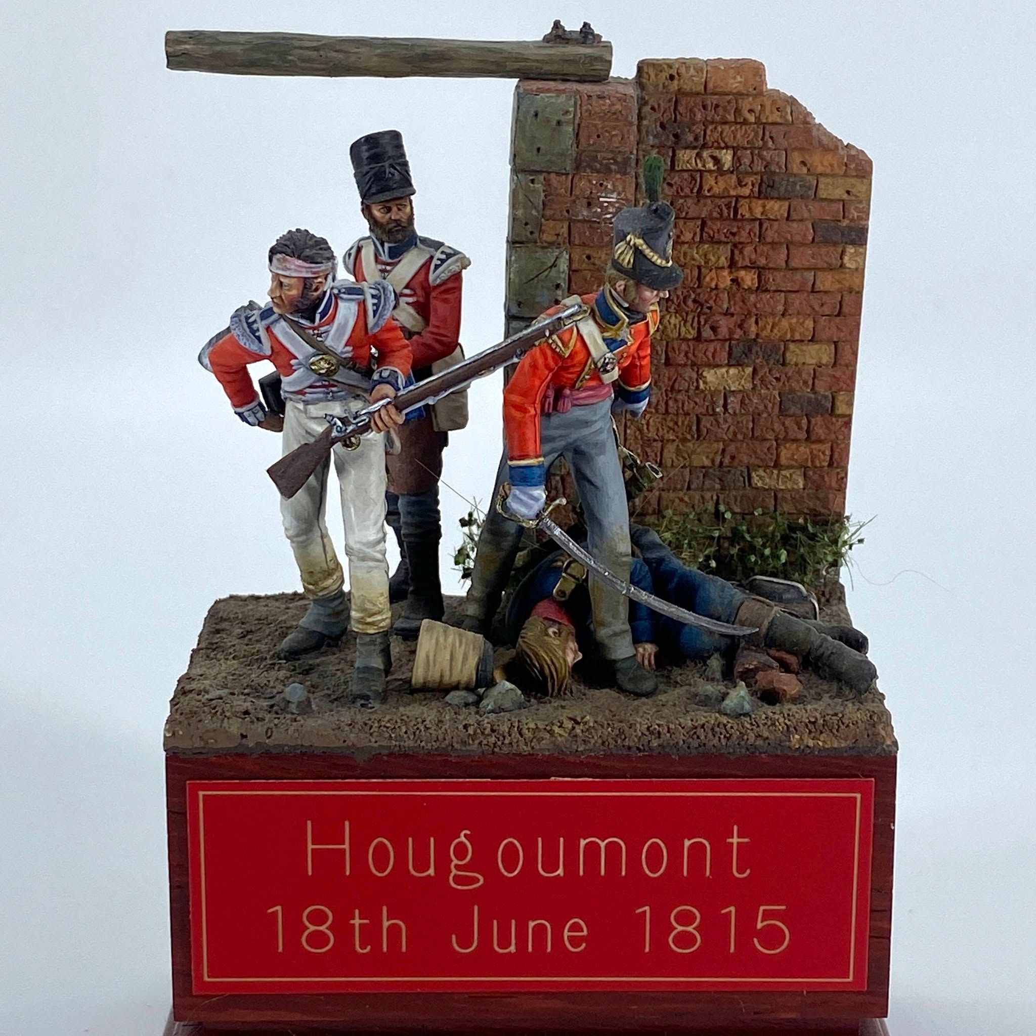 Diorama of three British redcoat infantrymen beside a ruined brick wall, one with a bandaged head, standing over a fallen French soldier.