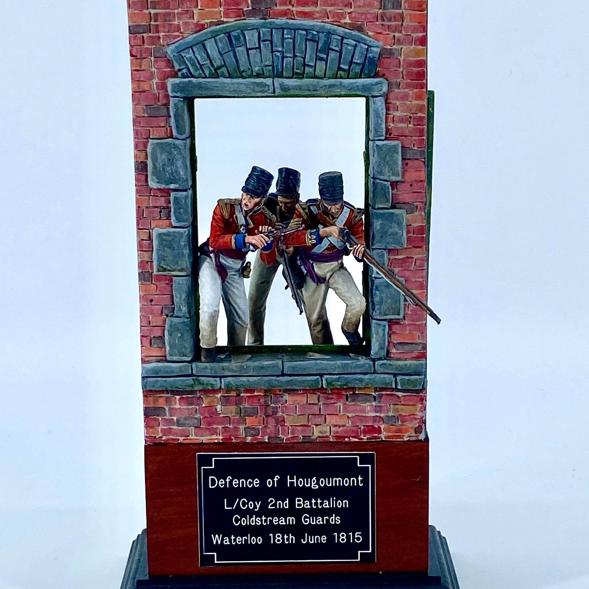 Vignette of three Coldstream Guards in red coats firing muskets through the window of a brick farm building.