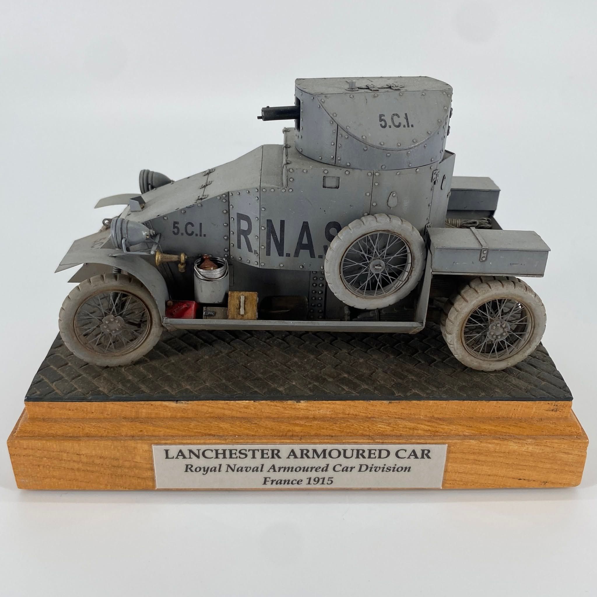 Grey First World War armoured car lettered R.N.A.S. on the hull side, with spoked wheels and a single turret, on a cobbled base.
