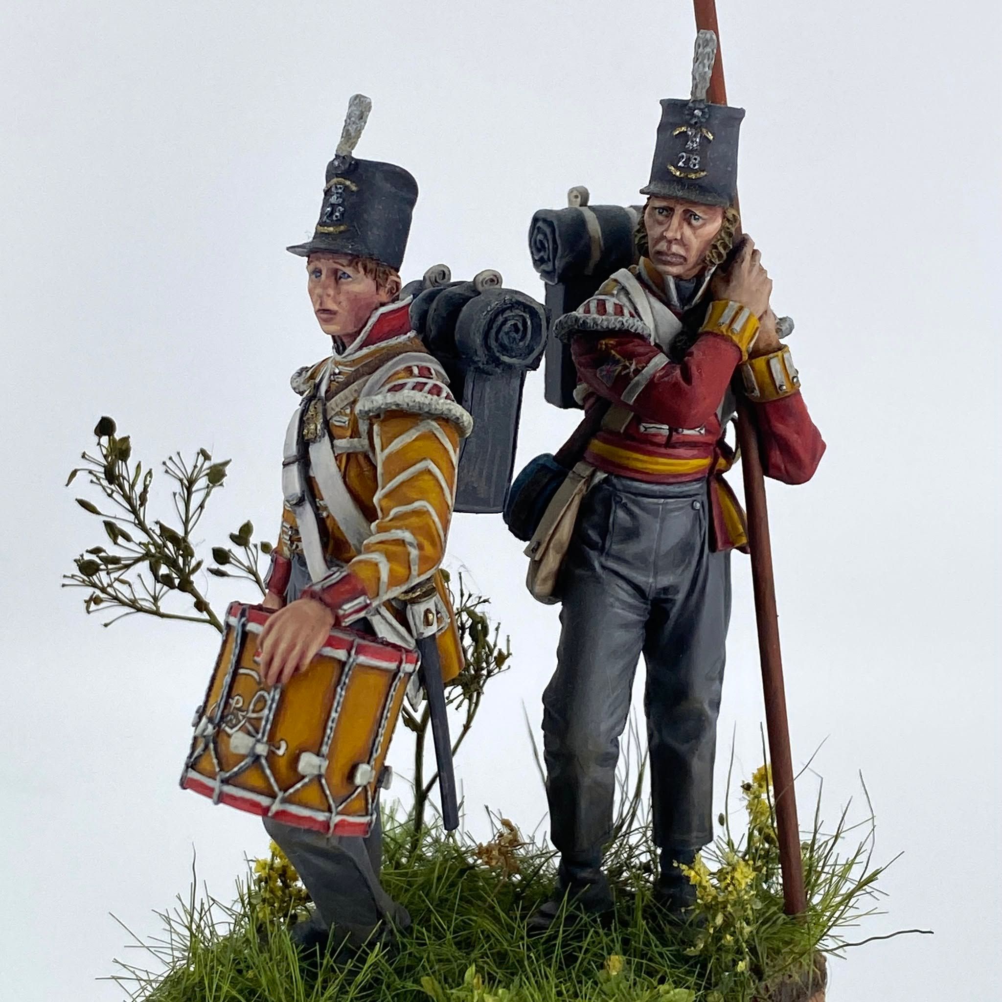 Two Napoleonic British infantrymen on a grassy base: a young drummer in a yellow-faced coat with a painted drum, and a private in a red coat shouldering a musket.
